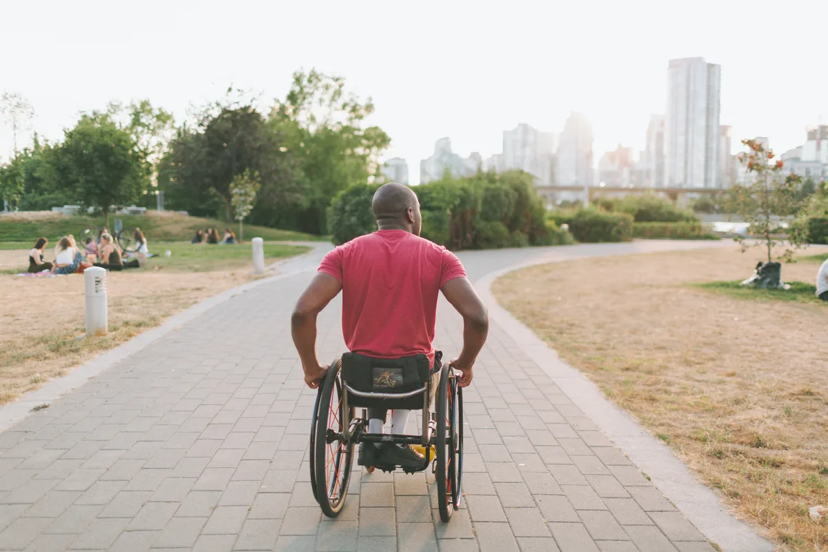 Homme athlétique en fauteuil roulant sur un sentier pavé, ville en arrière-plan