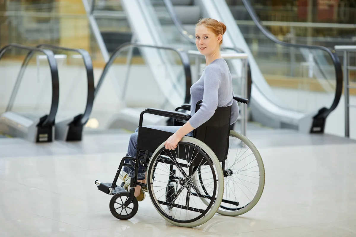 Femme en fauteuil roulant devant des escaliers mécaniques dans un centre commercial
