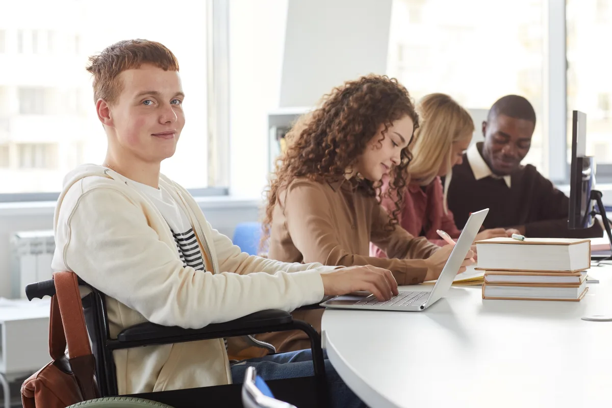 Groupe d’étudiants qui travaillent sur des portables, dont un en fauteuil roulant