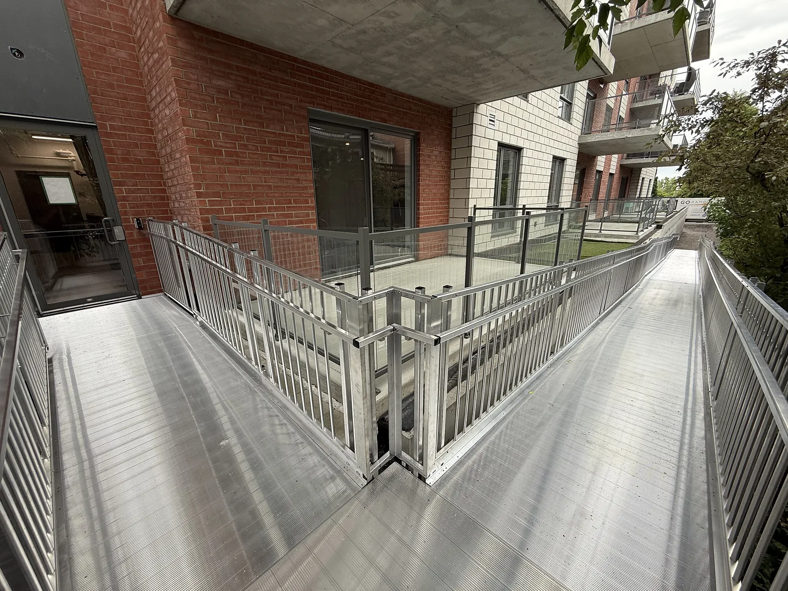 Rampe en aluminium avec palier et garde-corps à barrotins devant un immeuble d’habitation